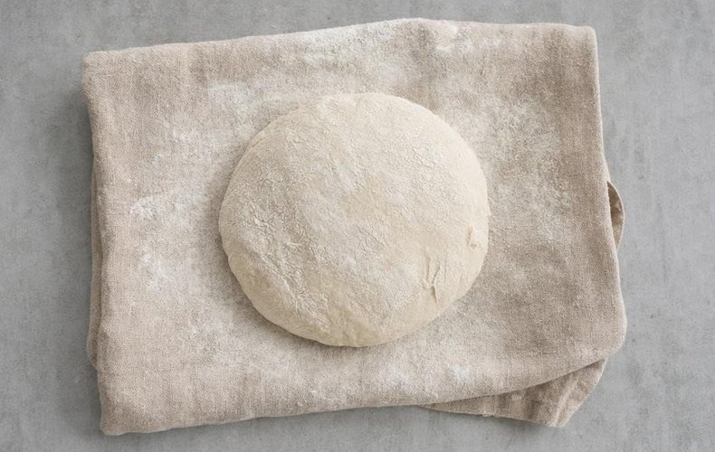 Mit Mehl bestäubter Brotteig ruht unter einem Geschirrtuch
